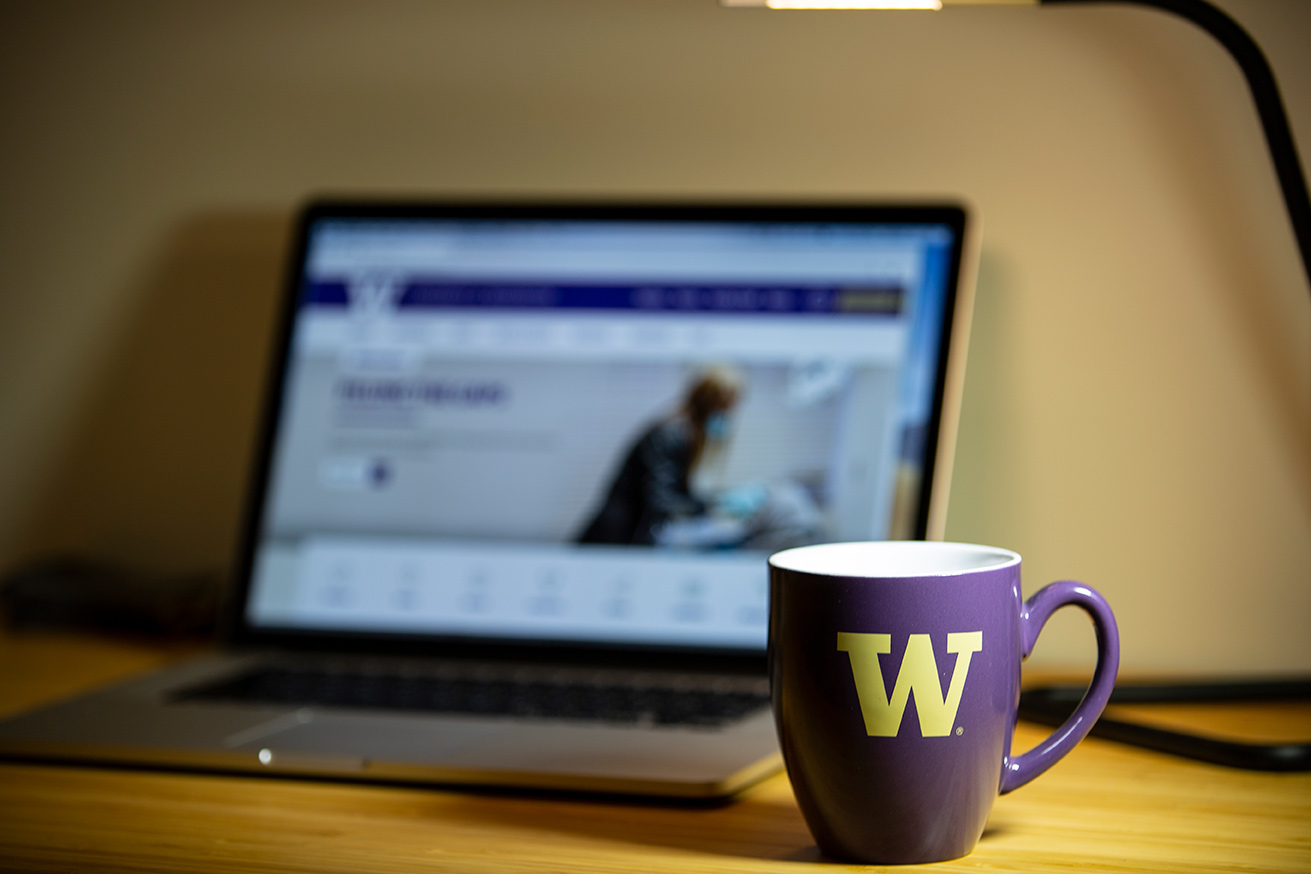Purple University of Washington mug on a desk in front of an open laptop