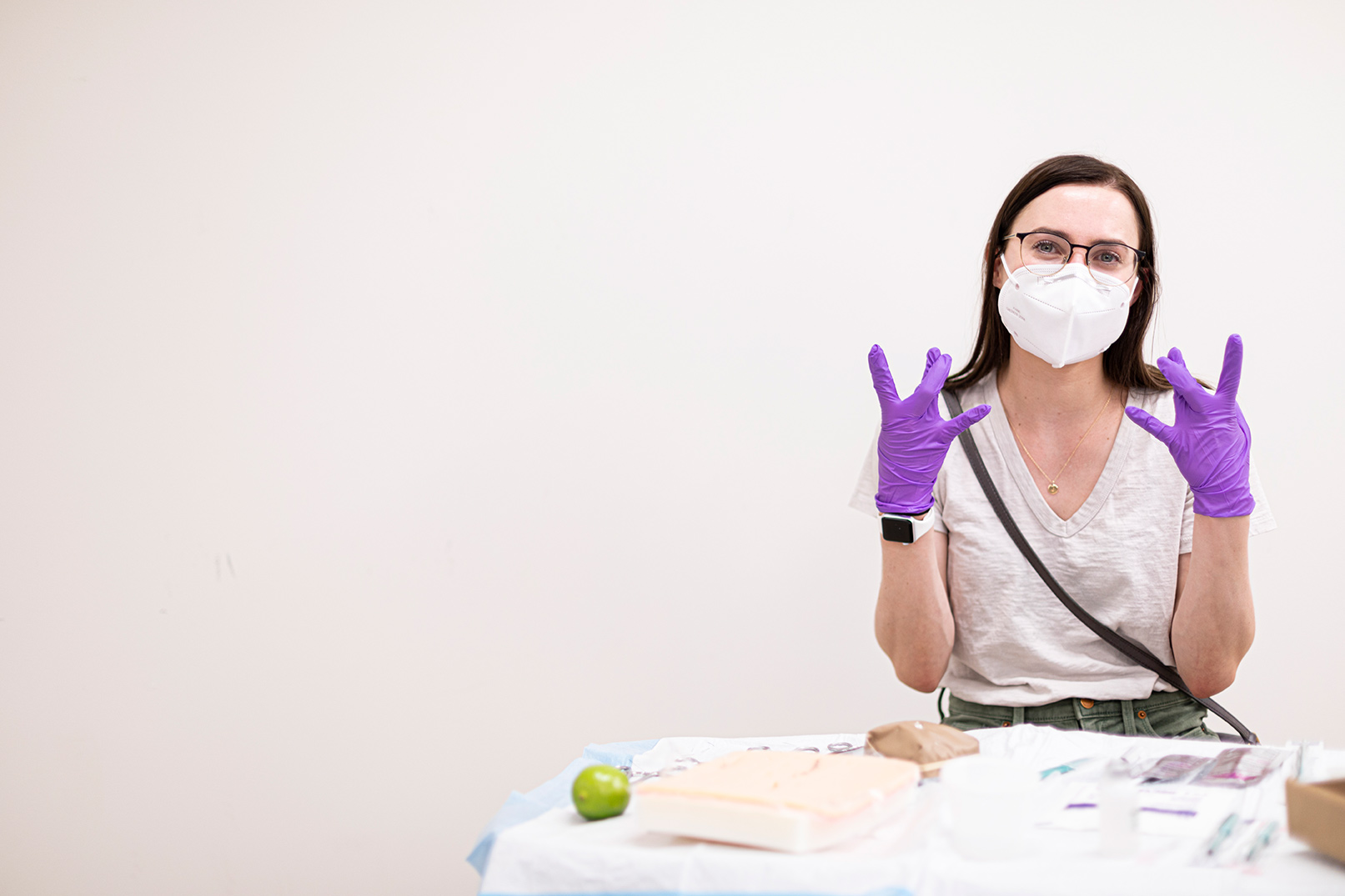 A nursing student in safety glasses and gloves making a W with her hand